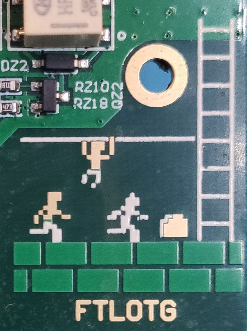 Close-up of a green circuit board with copper and silkscreen pixel art of a running figure, a ladder and green bricks, with the letters FTLOTG.